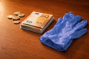 Euro-Scheine und Münzen neben einem blauen Latex-Einweghandschuh auf einem Holztisch – Symbol für die finanzielle Seite ambulanter Pflege